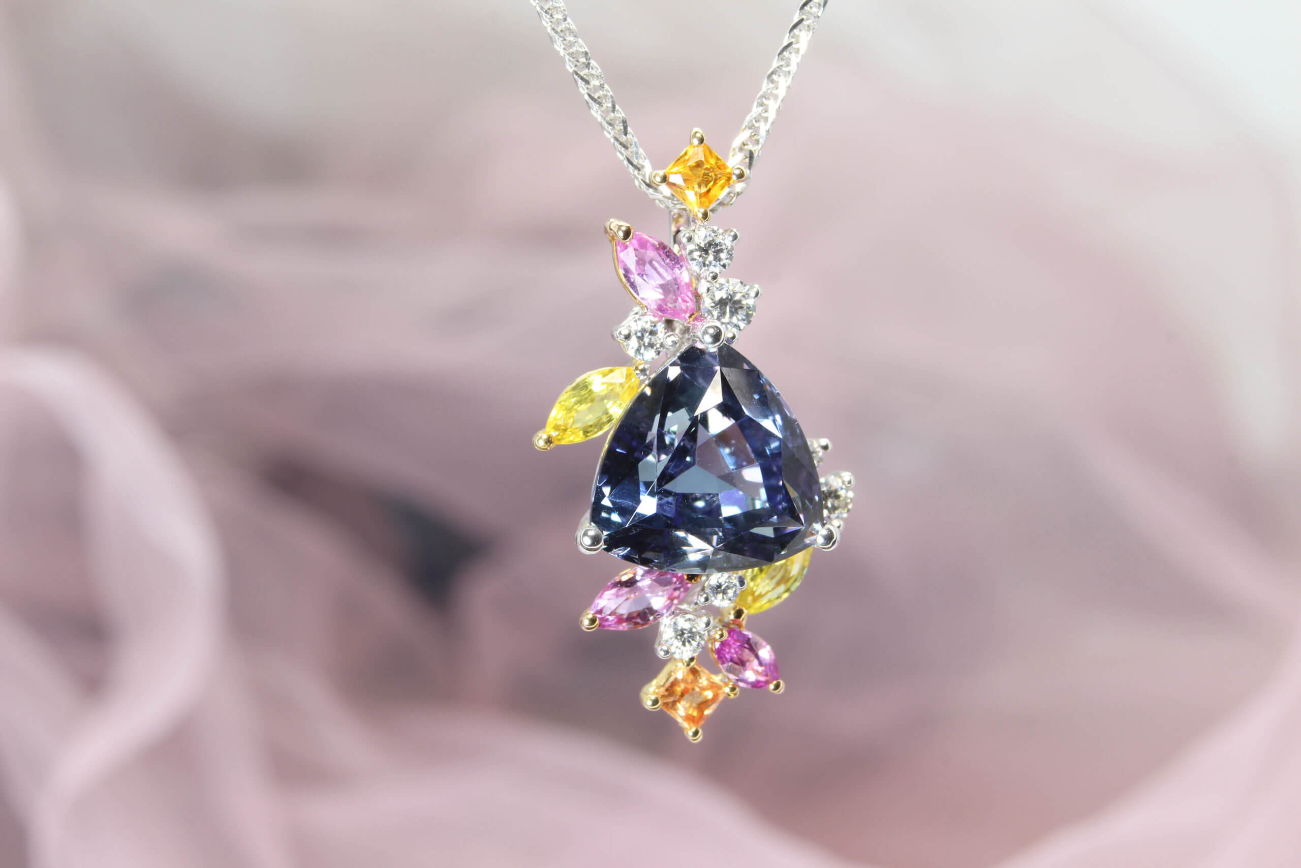 Tanzanite Pendant in unique trilliant shape customised with multiple coloured sapphire gemstone from pink, yellow to orange shade. The flora-style cluster of multi-shaped and colourful gemstones. Local Singapore Jeweller in customised jewellery and Wedding Jewellery with coloured gemstone.